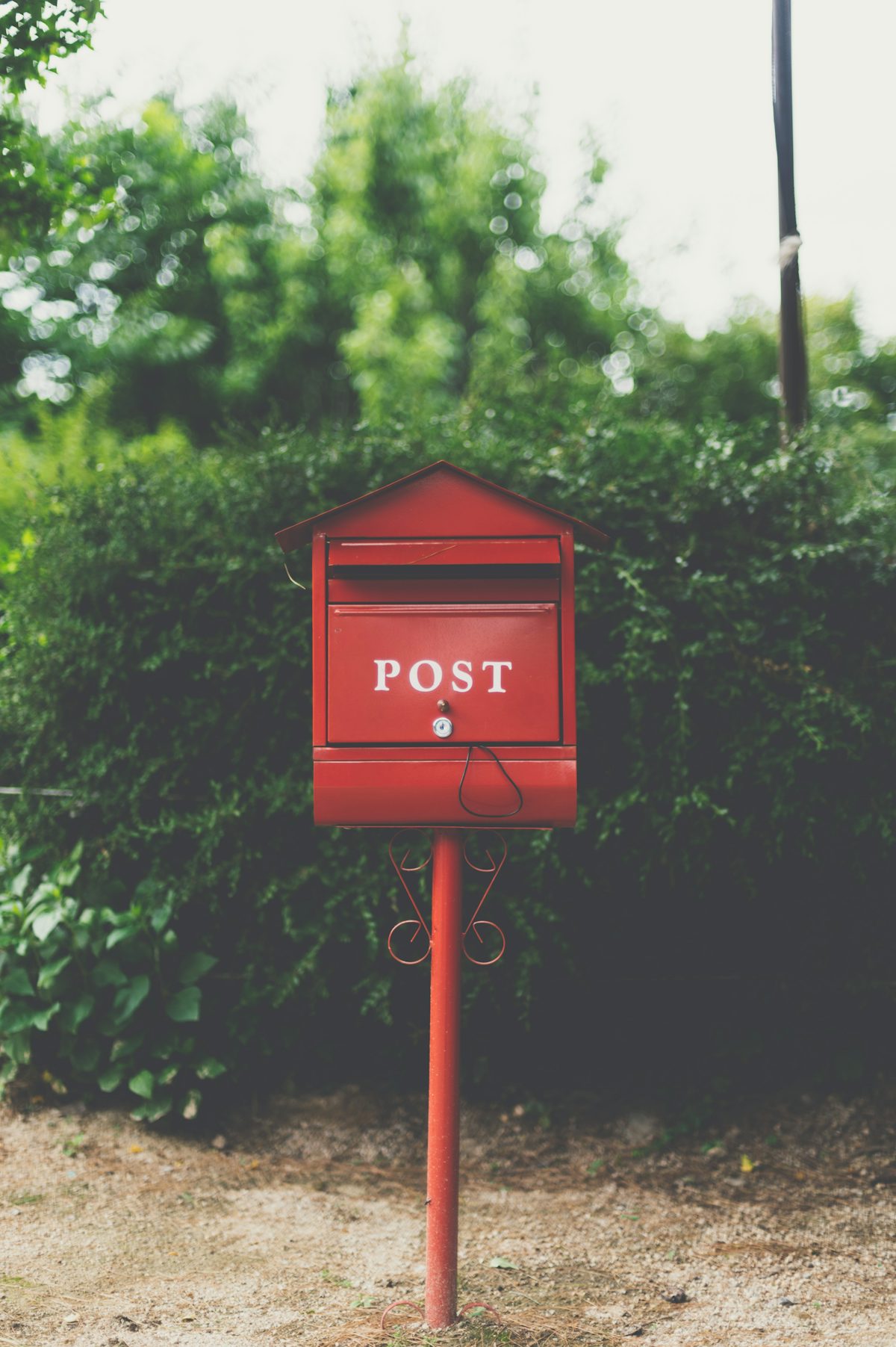A red POST mailbox on a post in front of a green hedge